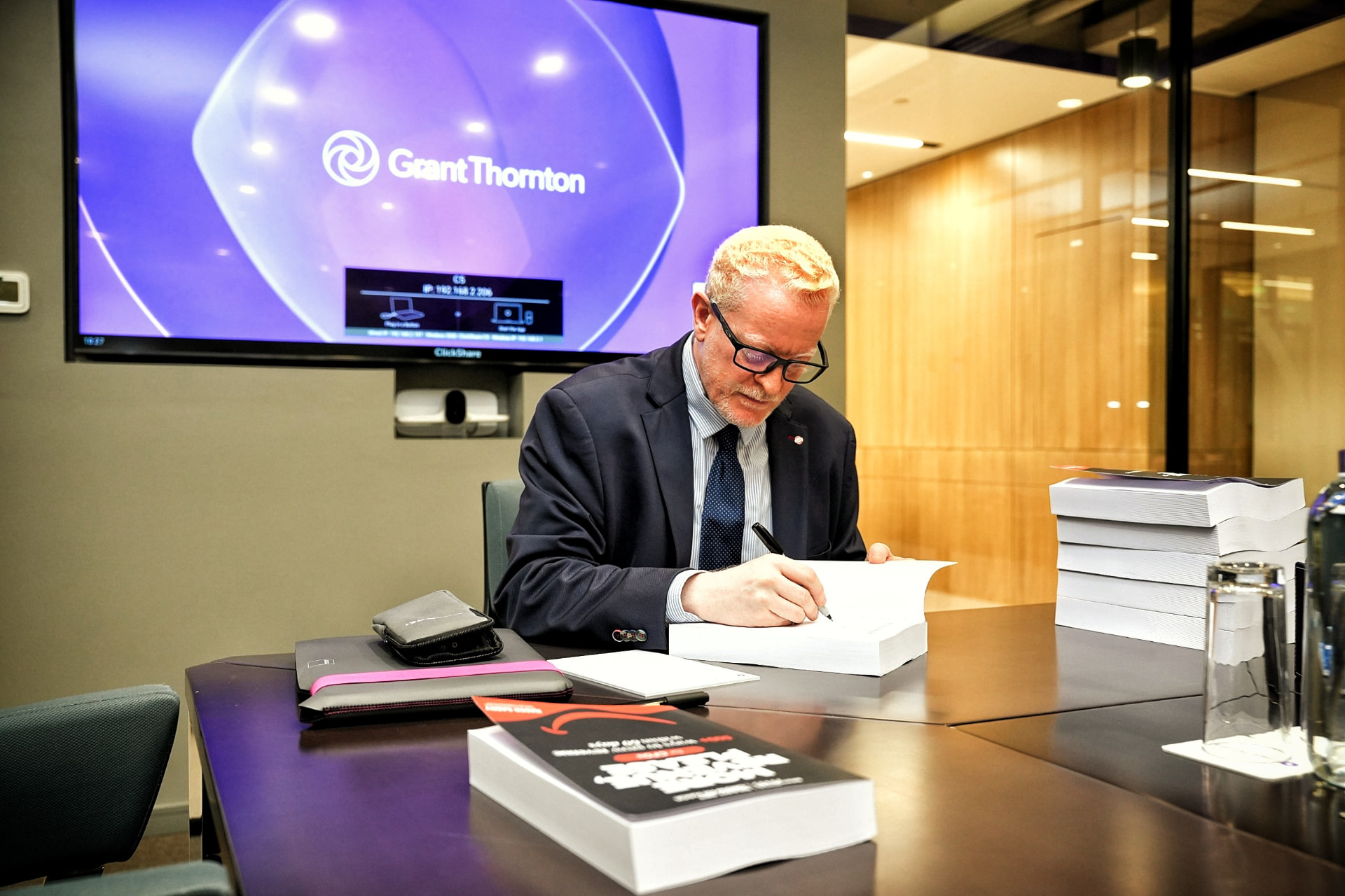 Nader Sabry signing copies of More Revenue, Please at a Grant Thornton UAE meeting room table